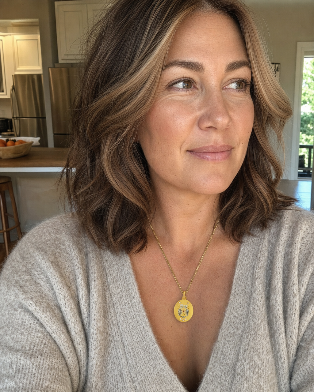 A woman in a beige sweater wearing a Peace Piece Elysian Skeletons hand-painted enamel pendant in her kitchen on a quiet afternoon